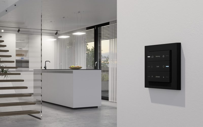 Modernes Smart-Home-Bedienfeld an einer weißen Wand in einer minimalistischen Küche, das einen aktuellen Überblick über Ihren Raum bietet, mit einer Glastreppe und großen Fenstern im Hintergrund. Modernes Smart-Home-Bedienfeld an einer weißen Wand in einer minimalistischen Küche, das einen aktuellen Überblick über Ihren Raum bietet, mit einer Glastreppe und großen Fenstern im Hintergrund.